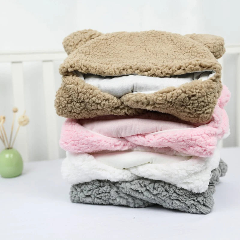 Une pile soignée de couvertures pour bébé Couverture bébé Nid D'Ange pliées et moelleuses dans des couleurs pastel et neutres sur fond clair, idéales pour le bain bébé et l'hygiène générale bébé de BABY-PREMA.