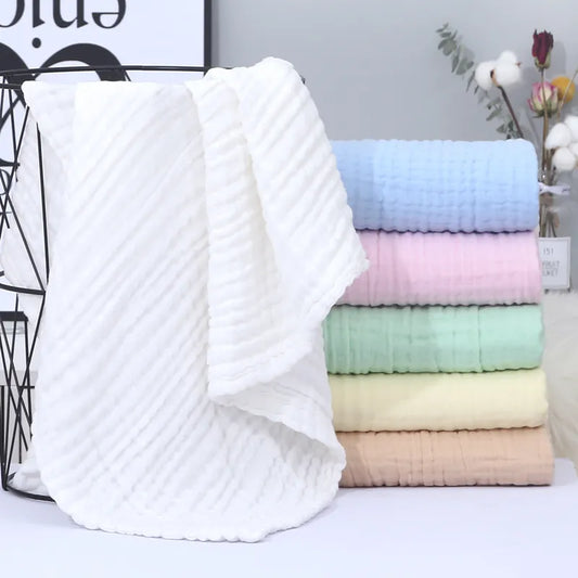 Une collection de serviettes Lange Bébé douces aux couleurs pastel soigneusement empilées avec une serviette blanche élégamment drapée sur un support en fil noir, suggérant une salle de bain confortable et organisée ou une armoire à linge BABY PREMA.