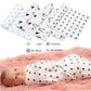 Un bébé paisible enveloppé dans une élégante couverture Baby Prema en Mousseline de Coton pour Bébé noire et blanche avec des motifs modernes, reposant sur une surface rose tendre, avec une collection de langes à motifs similaires soigneusement pliés à proximité. Les accessoires indiquent