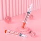 Deux seringues BABY-PREMA surdimensionnées remplies de liquide orange sur fond rose, comportant des sphères rose tendre et un mur rayé, représentant un concept médical stylisé et surréaliste lié au bébé prématuré.