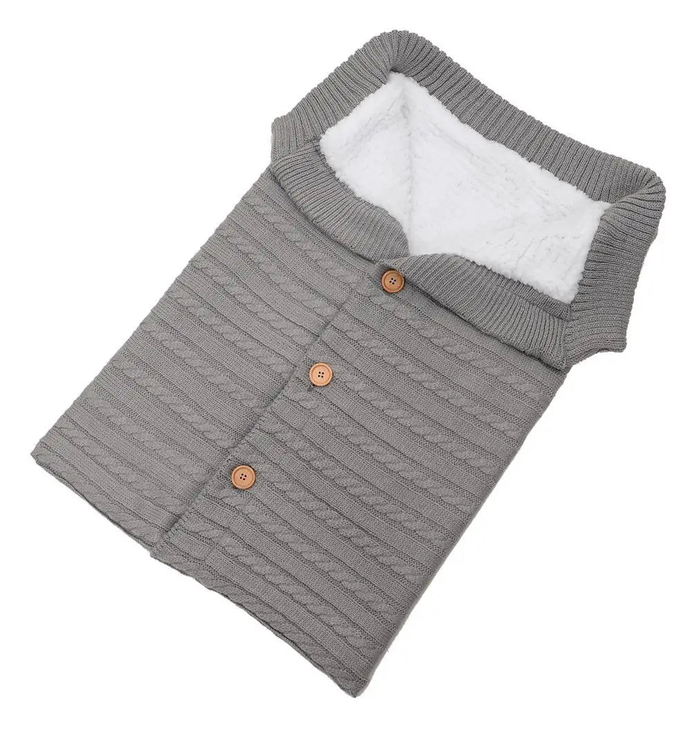 Un pull bébé gris côtelé avec une doublure polaire blanche douillette et des boutons en bois soigneusement pliés sur fond blanc de la Couverture en Polaire Ultra Doux et Moelleux de BABY PREMA.