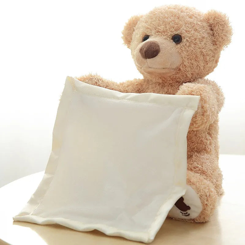 Une peluche Doudou Ours Peluche Musical Chantant "Peekaboo" de BABY PREMA assis à côté d'un oreiller dodo blanc, dégageant une ambiance cosy et attachante.