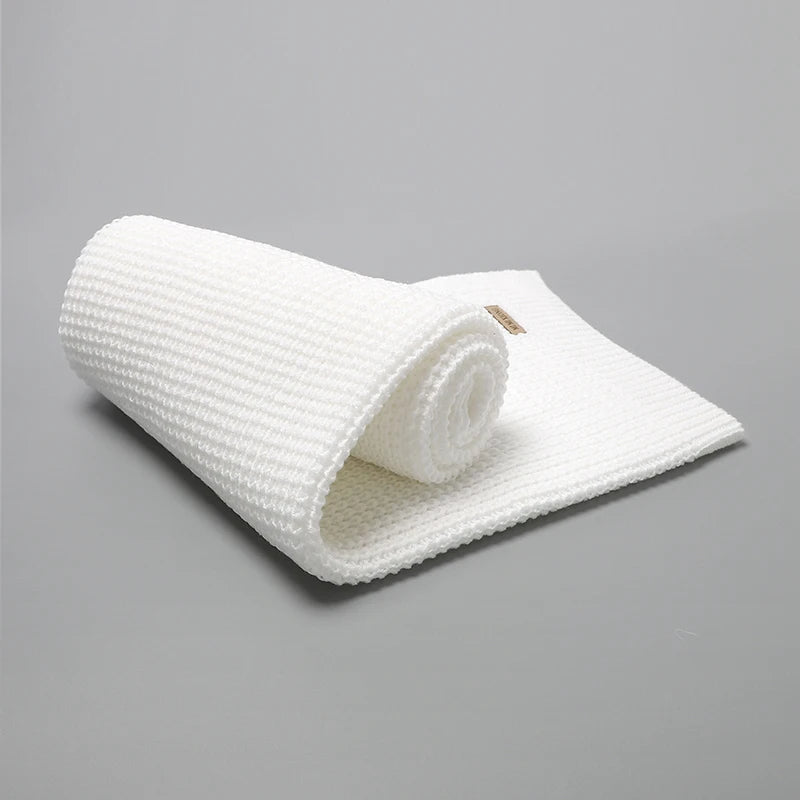 Une serviette blanche texturée partiellement déroulée sur une surface grise, rappelant une Couverture Bébé Tricot Fin 90*70cm - Baby-Prema de Baby-Prema qui offre douceur et confort toute l'année.