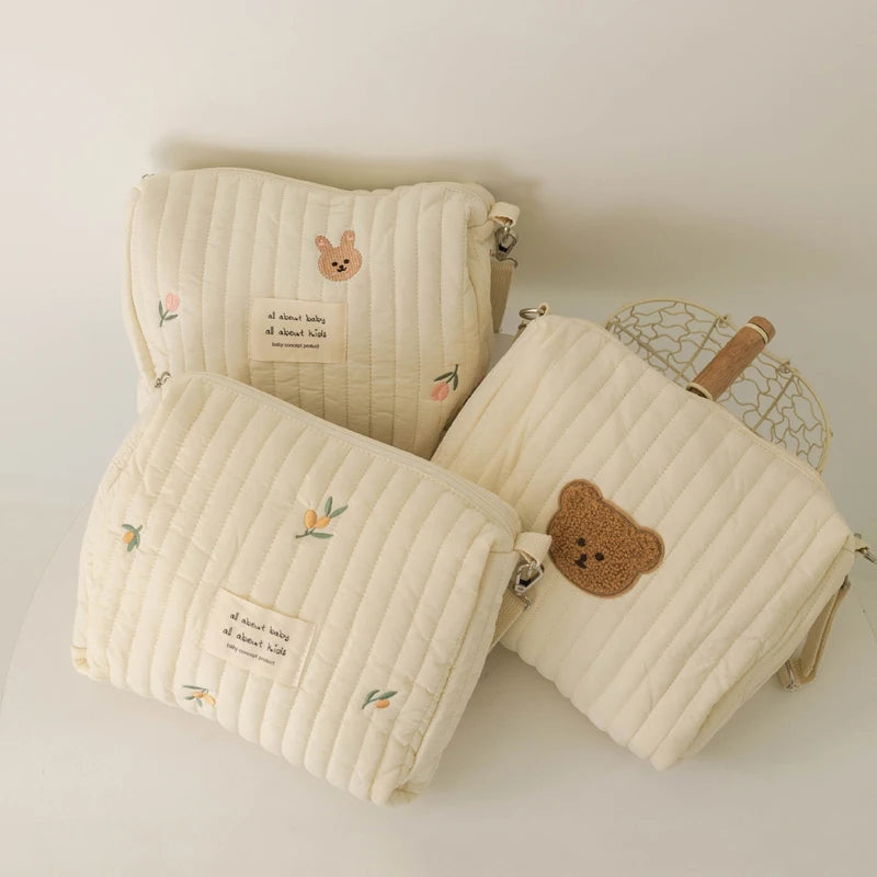 Trois pochettes Sac à Couches en Coton en tissu doux et matelassé avec des motifs floraux pastel et de jolies broderies d'animaux sur fond neutre, parfaites pour les essentiels de maternité pour mon bébé de BABY PREMA.