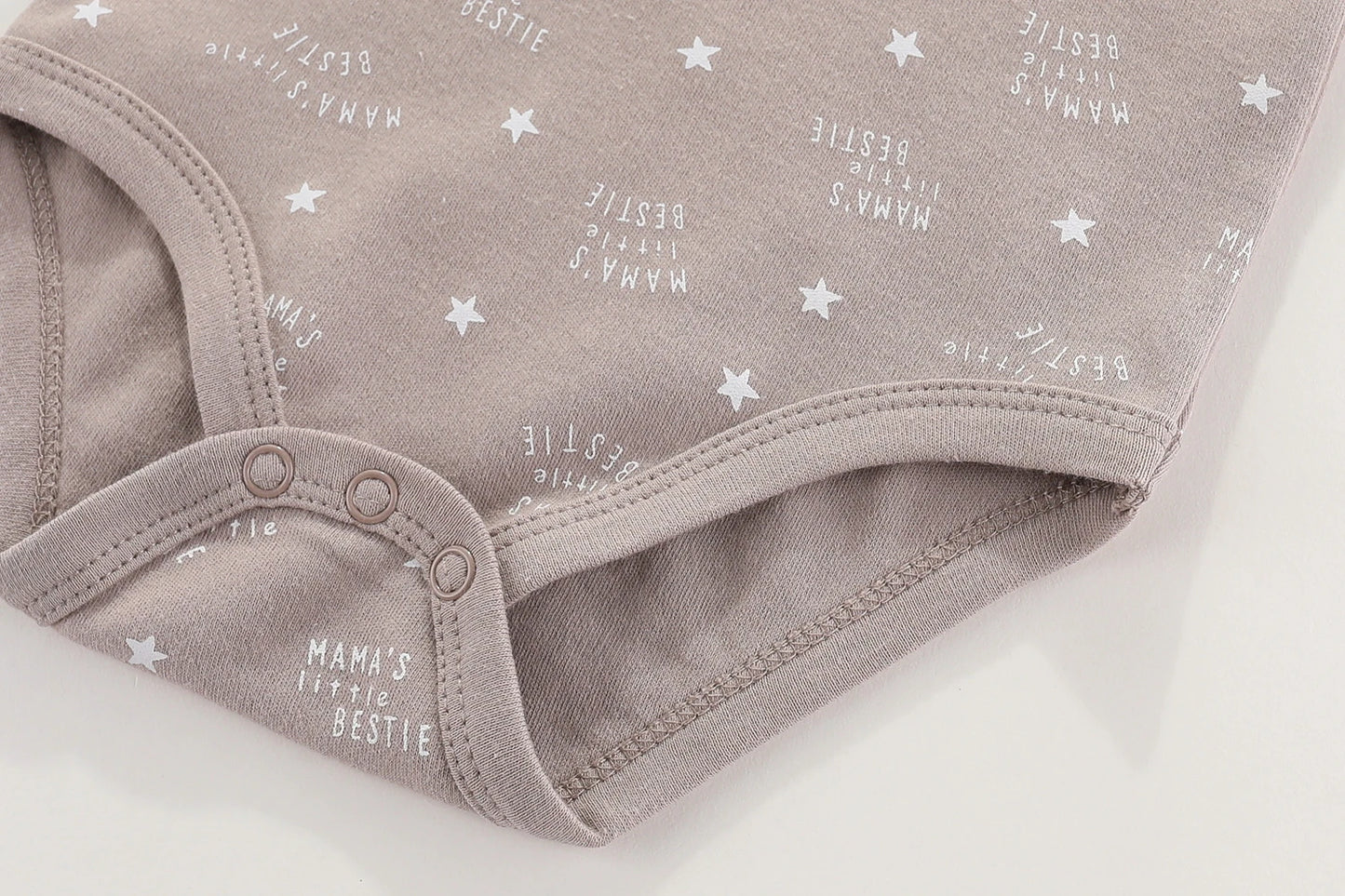 Gros plan d'un Lot 6 Body Coton Bébé Manches Courtes marron clair de BABY PREMA avec des boutons-pression, des motifs d'étoiles blanches et le texte "MAMA'S Little BESTIE" dispersé sur le tissu. Fabriqué à partir de coton doux, ce body pour bébé comporte des manches courtes pour plus de confort.