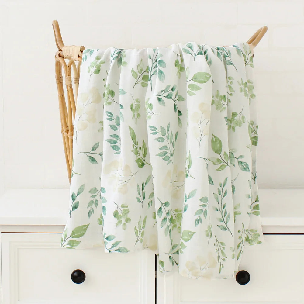 Un tissu floral avec une feuille et un motif BABY PREMA Couverture Bébé en Coton et Bambou Bio drapé sur une tige en bois, suggérant un style frais et naturaliste pour la décoration de chambre d'enfant.