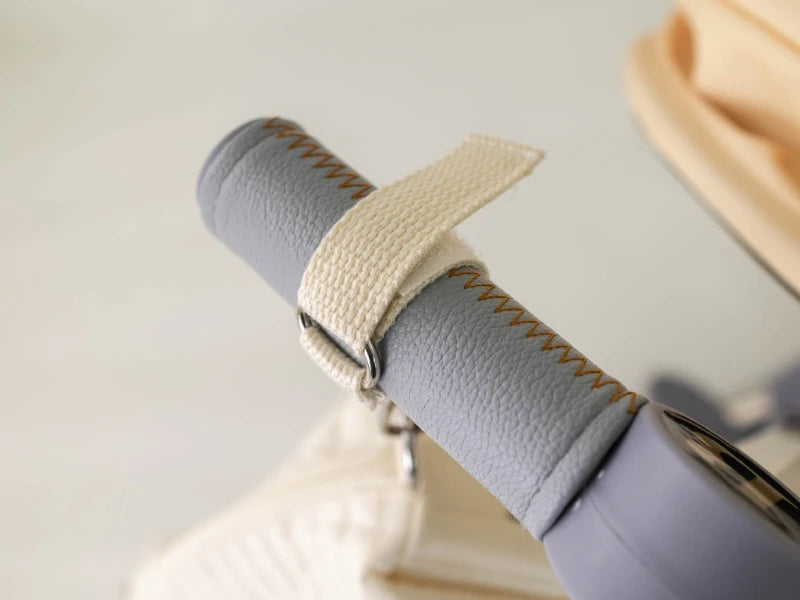 Élégant bracelet en cuir avec coutures crème sur un Sac à Couches en Coton pour poussette pour enfants gris clair enroulé par BABY PREMA.