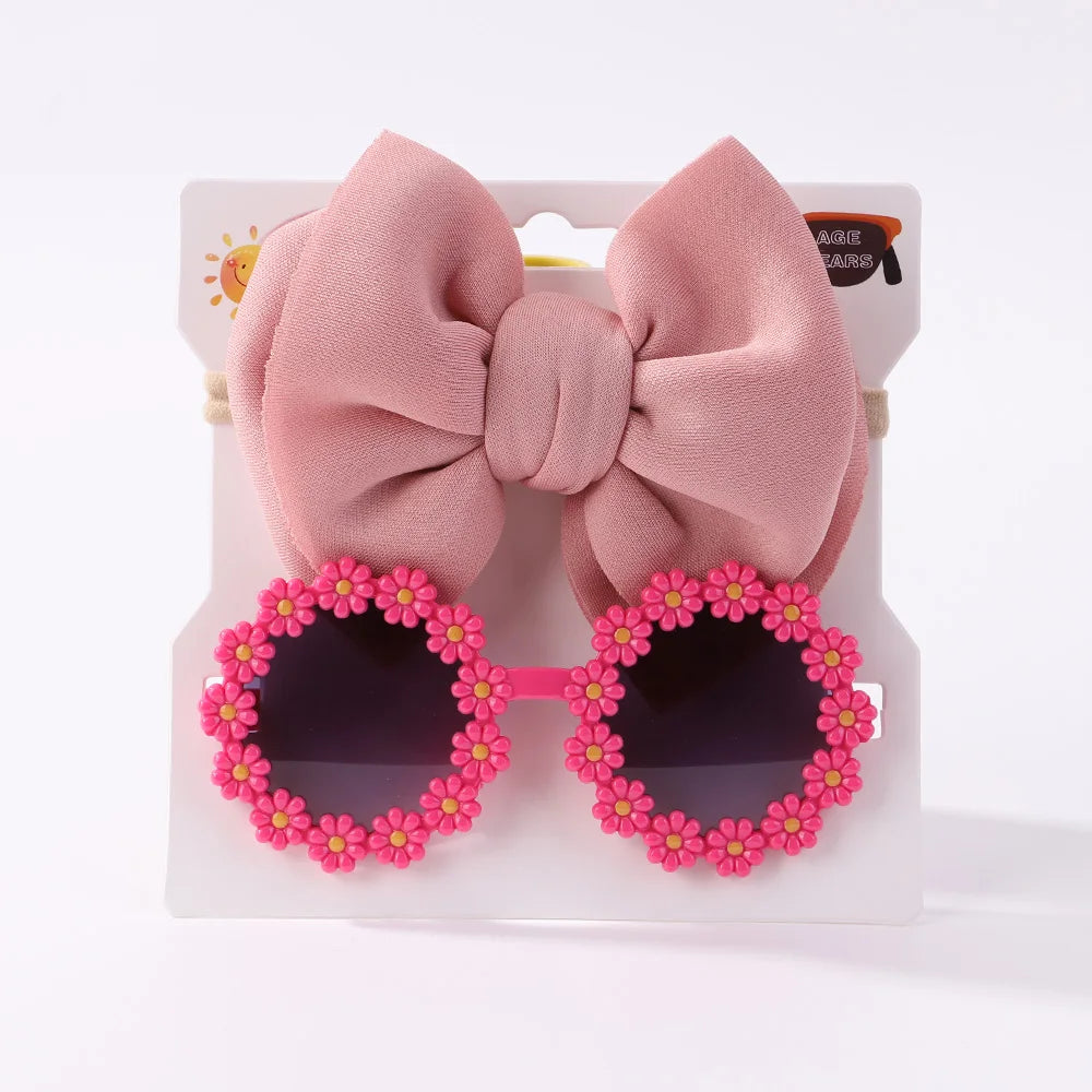 Une paire de Set d'Accessoires Bébé ronds | Lunettes de Cheveux pour Bébé avec monture à fleurs roses et accessoire grand nœud rose affichés sur fond blanc par BABY PREMA.