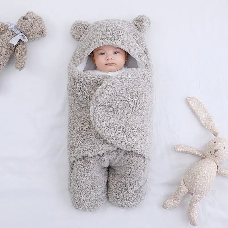 Un bébé douillet enveloppé dans une gigoteuse moelleuse en forme d'ours avec des peluches à ses côtés, entouré de la Couverture Doux Bébé 0-7 Mois de BABY-PREMA.