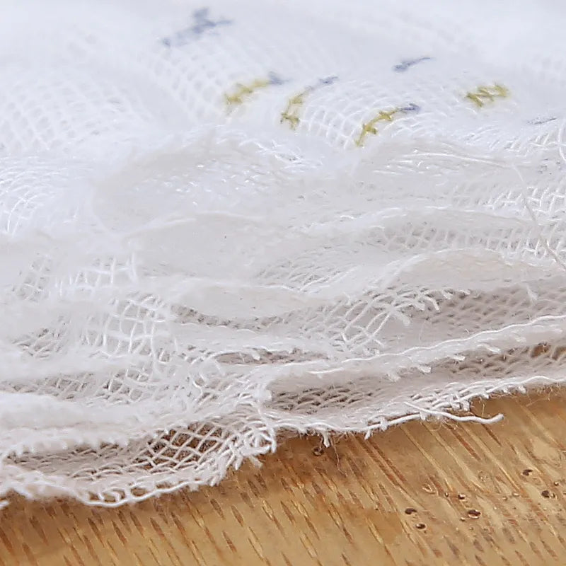 Gros plan d'un tissu blanc BABY PREMA Lange Bébé effiloché avec de délicates broderies sur une surface en bois.