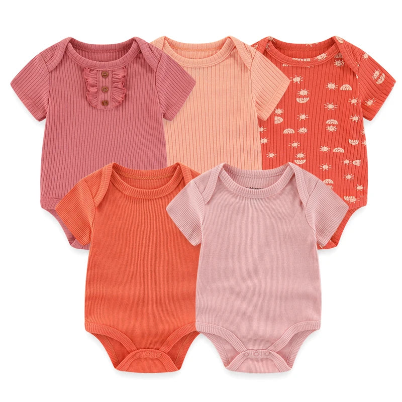 Cinq combinaisons pour bébé à manches courtes dans différentes nuances de rose et de pêche sont présentées. Chaque grenouillère, confectionnée à partir du Lot de 5 Bodys Coton Agréables & Conforts de BABY PREMA, présente des designs uniques comprenant des boutons, des volants et des motifs, assurant douceur et confort à votre tout-petit.