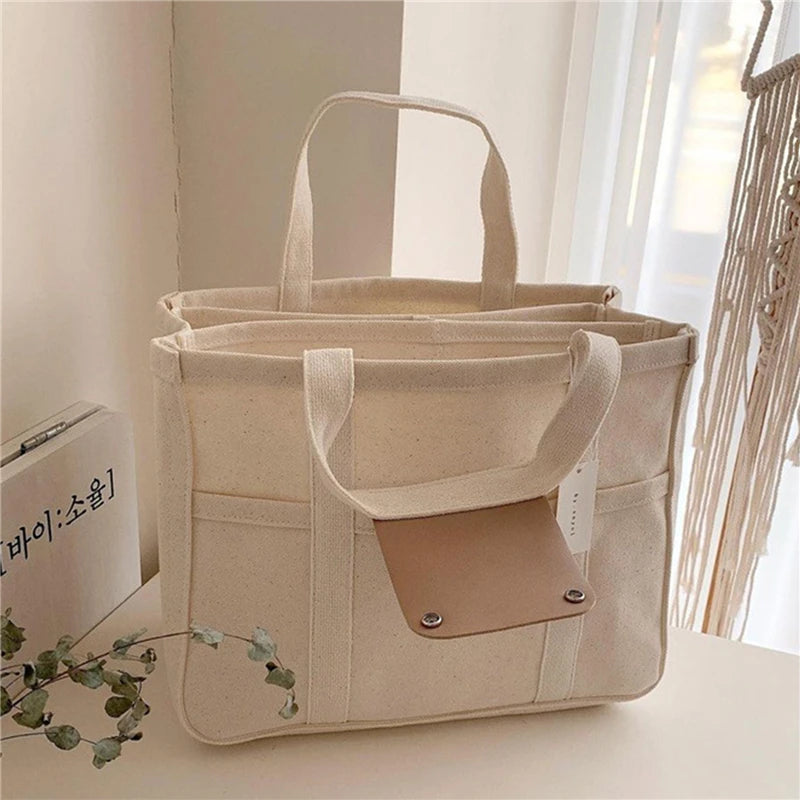 Sac cabas en toile beige avec plusieurs poches et fermeture à bouton-pression, parfait pour "BABY-PREMA Sac à couches pour bébé | Sac à Main Imperméables", exposé dans un décor intérieur cosy.