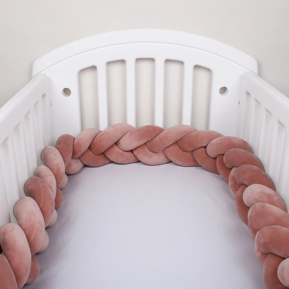 Un lit bébé douillet avec des côtés à lattes blanches. À l'intérieur du berceau, un Tour de lit bébé 4M tressé de BABY PREMA sert de tour de lit doux et tressé de couleur rose poudré, tapissant le périmètre intérieur. Le matelas est recouvert d'un drap blanc uni.