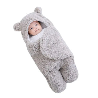 Un bébé emmitouflé dans une couverture Cocon pour Bébé douillette sur le thème de l'ours de BABY-PREMA, regardant avec des yeux curieux parmi les nécessaires pour bébé.