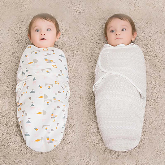 Deux adorables bébés bien emmaillotés dans des couvertures, allongés côte à côte et regardant vers le haut avec des yeux curieux, entourés de leur jolie BABY PREMA Couverture Bébé Cocoon 100% Coton.