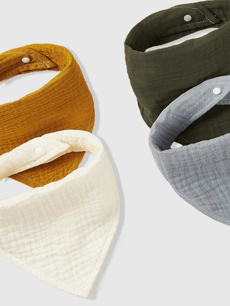 Une collection de quatre Bavoirs bandana Coton Bio | Bébé de la marque BABY PREMA dans des tons terre et gris pastel, arrangés en cascade sur un fond blanc, parfaits pour garder les