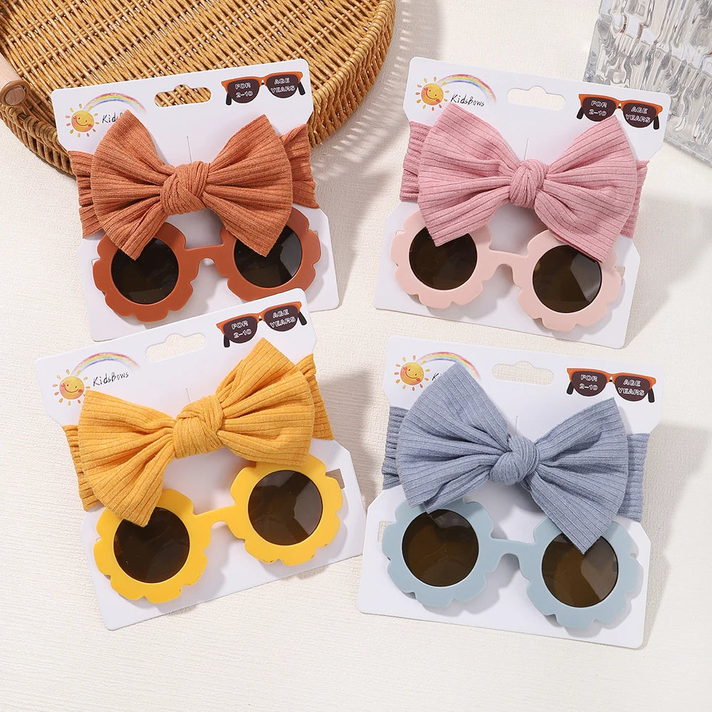 Quatre ensembles de Set d'Accessoires Bébé | Les Lunettes de Cheveux pour Bébé de BABY PREMA sont présentées, chacune avec un bandeau à nœud en nylon assorti. Les ensembles sont disponibles en couleurs : orange, rose, jaune et bleu. Les lunettes de soleil présentent une monture ronde.