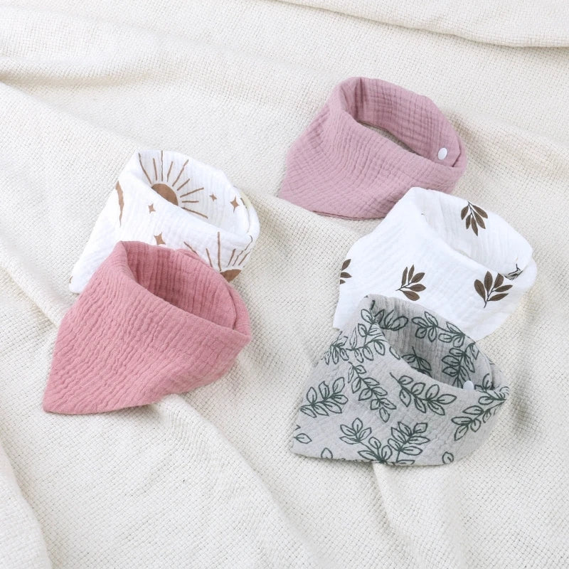 Cinq bavoirs en mousseline de coton pour bébé BABY-PREMA sont disposés sur un tissu doux de couleur crème. Les modèles de bavoirs incluent du rose uni, du violet uni, du blanc avec des motifs de soleil, du blanc avec des motifs d'oiseaux et du gris avec des motifs de feuilles. Fabriqué en mousseline de coton pour plus de douceur, chaque bavoir bébé est doté d'un tissu texturé et d'une fermeture à bouton-pression pour des vêtements de protection pratiques.