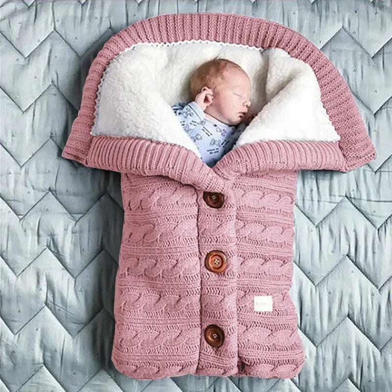 Un nouveau-né serein dort paisiblement dans une gigoteuse douillette en tricot ressemblant à un pull bien boutonné, accessoire indispensable à l'hygiène de bébé. Il s'agit de la Couverture de Poussette Pour Bébé BABY PREMA.