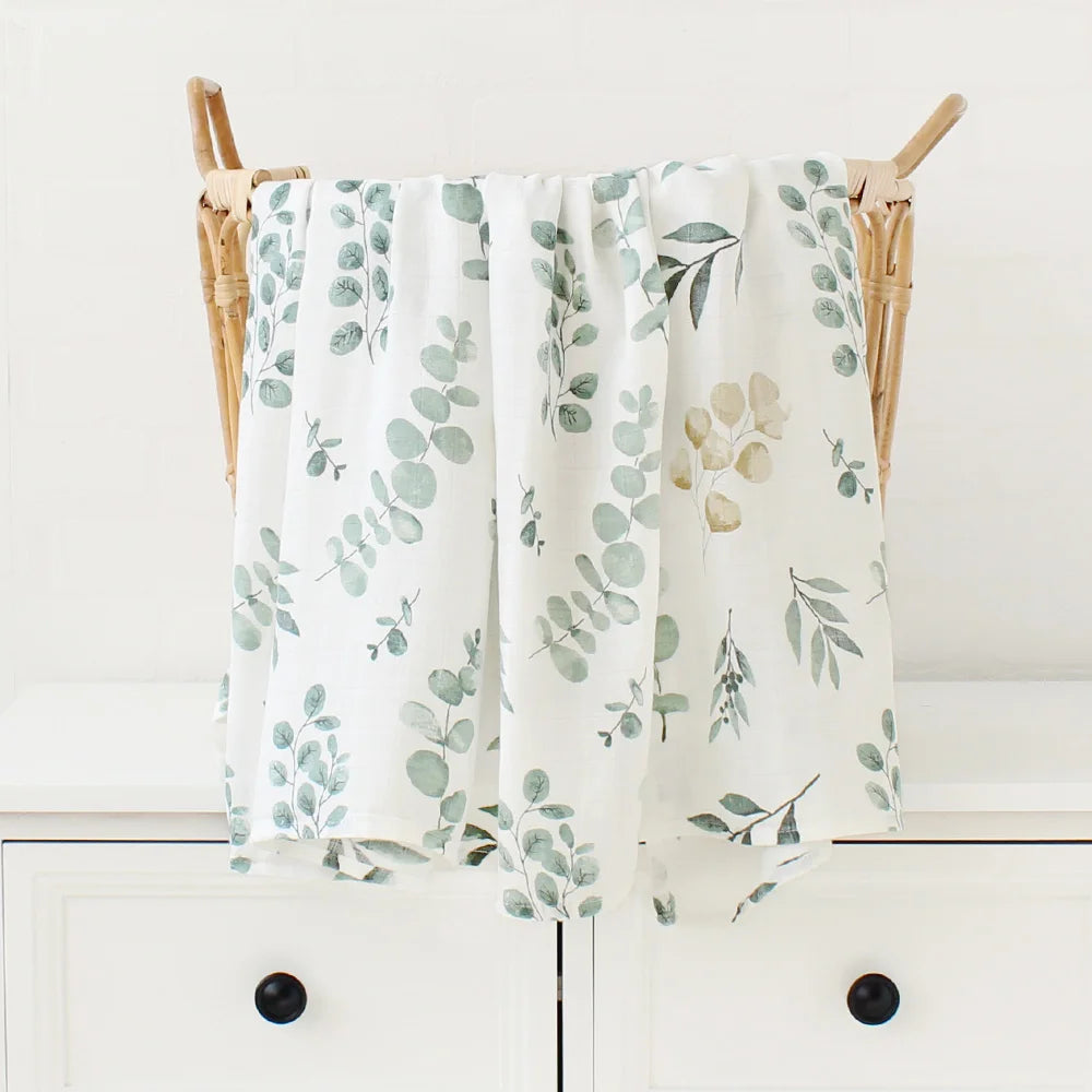 Une paire de serviettes Couverture Bébé en Coton et Bambou Bio aux motifs frais et élégants avec des motifs de feuilles, drapées sur une chaise en bois dans un cadre de cuisine lumineux et propre, servant d'accessoires bébé BABY PREMA pratiques.