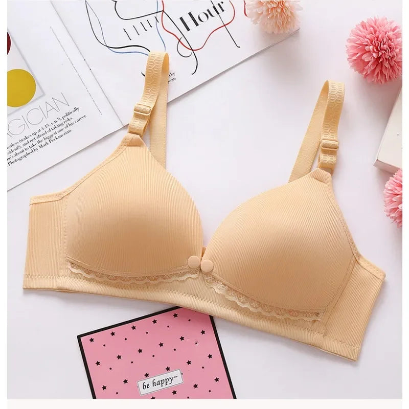 Un soutien-gorge Elégant Soutien d'Allaitement beige avec des bonnets moulés et des détails en dentelle, affiché sur une surface blanche aux côtés de fleurs décoratives et d'une joyeuse papeterie « enfant ».