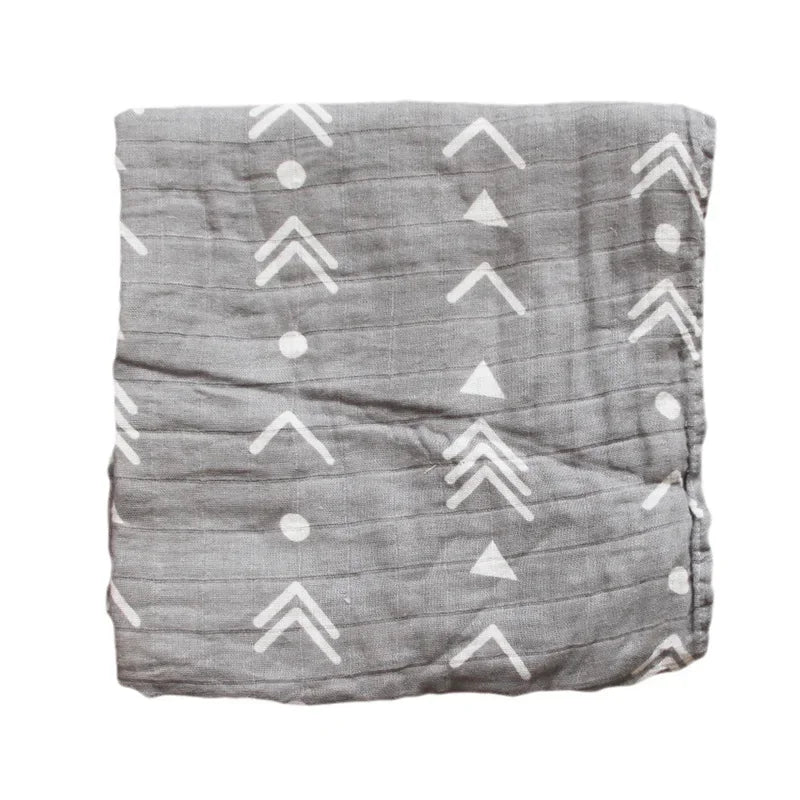Un tissu gris froissé avec un motif de flèches et de points blancs, suggérant un design minimaliste ou tribal pour la Couverture en Mousseline de Coton pour Bébé de BABY PREMA, présentée sur un fond blanc.