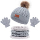 Un ensemble d'accessoires d'hiver douillet comprenant un BABY PREMA Ensemble 3Pièces Bonnet Gants pour Bébé avec un pompon en fausse fourrure, des gants gris assortis pour un enfant et un cache-cou avec une doublure intérieure en peluche.