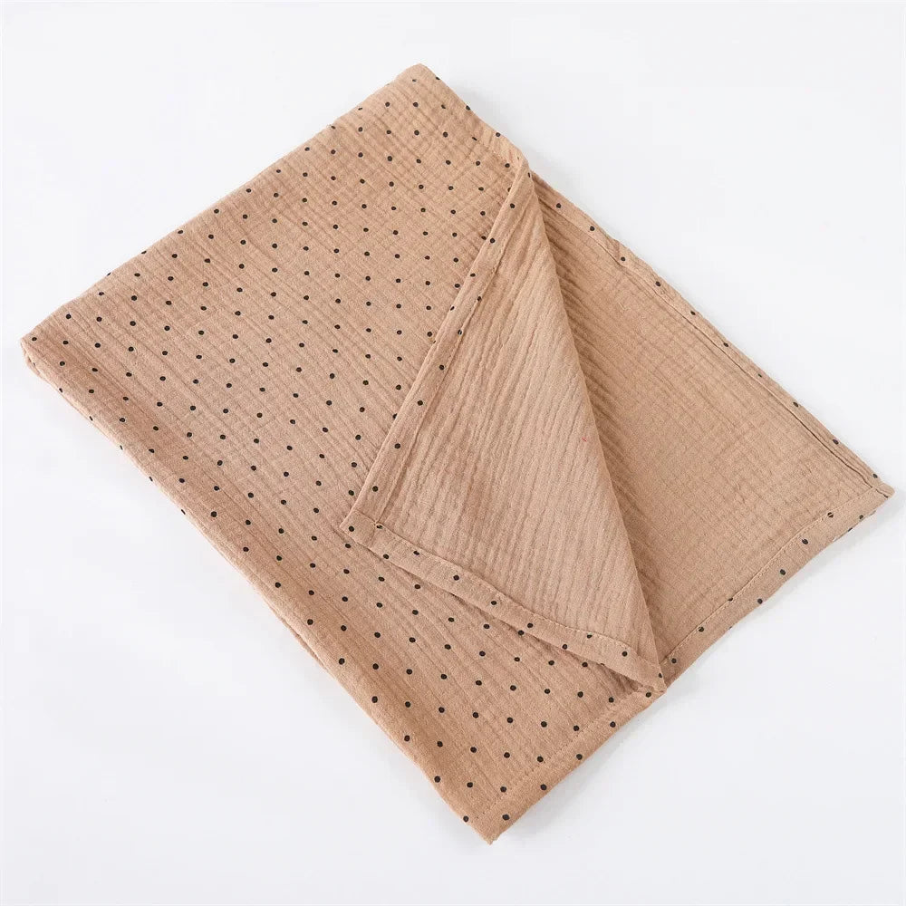 Une pochette de costume beige soigneusement pliée avec un motif de petits points noirs, affiché sur un fond blanc, parfaite comme accessoire pour la Couverture Emmaillotage en coton pour Bébé de BABY PREMA.