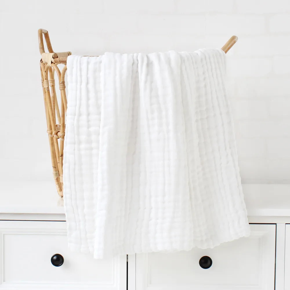 Une couverture dodo BABY PREMA texturée en peluche blanche drapée sur un porte-serviettes en bois de style échelle sur un fond de cuisine lumineux.