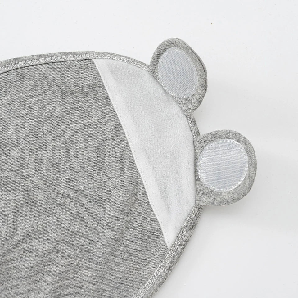 Couverture Bébé Emmaillotage grise de BABY PREMA avec des détails d'oreilles décalés et un design bicolore sur fond uni.