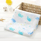Une couverture pour bébé BABY PREMA blanche et douce avec un motif joyeux de baleines bleues et d'étoiles jaunes, soigneusement placée à côté d'un panier en osier dans un décor de chambre de bébé lumineux et propre.
