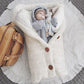 Un bébé paisible niché dans une couverture de poussette pour bébé douillette et boutonnée de BABY PREMA à côté d'un sac en cuir rempli de nécessaire pour bébé, respirant chaleur et confort.