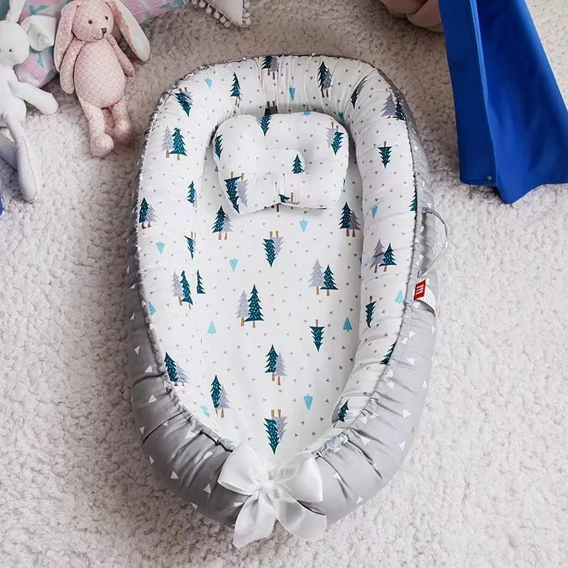 Un Lit de Bébé portable Nid de Cocoon douillet avec un motif sur le thème de la forêt, entouré de peluches et d'une couverture, créant un espace tranquille pour qu'un bébé prématuré puisse se reposer de BABY-PREMA.