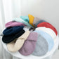 Une collection de bonnets colorés Bonnet Angora Pour Maman disposés en demi-cercle sur une surface blanche, mettant en valeur une variété de couleurs pastel et audacieuses de BABY PREMA.