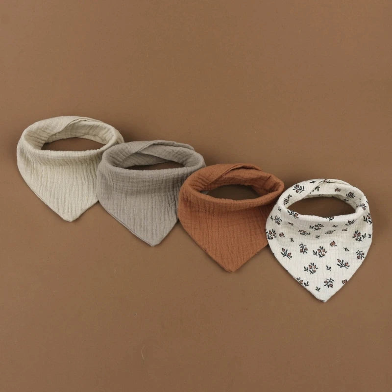 Quatre bavoirs en tissu sont exposés sur un fond marron. Ce lot de 4 bavoirs se décline en beige, gris clair, marron et blanc avec un motif floral noir. Chaque Bavoirs en mousseline coton pour bébé de BABY-PREMA est confectionné en mousseline de coton douce et présente une forme triangulaire avec une ouverture de cou arrondie.