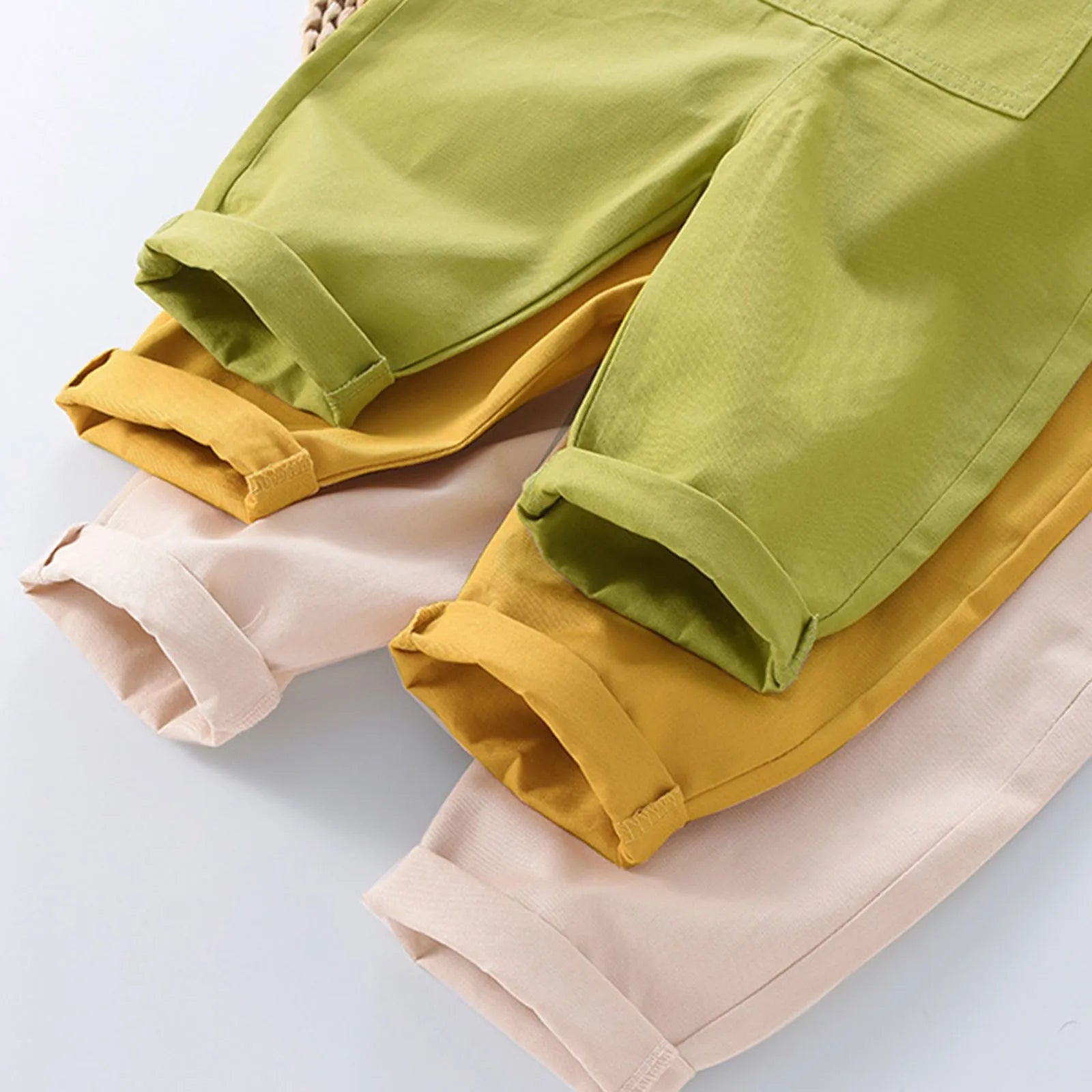 Trois pantalons retroussés de différentes couleurs (beige, jaune moutarde et vert olive) sont disposés sur une surface plane blanche, parfaits pour être associés à n'importe quelle Salopette BABY-PREMA Bébé Unie.