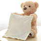 Une peluche Ours Musical "Peekaboo" assise avec une petite couverture blanche, parfaite pour un enfant prématuré, drapée sur ses genoux.