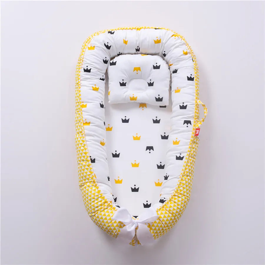 Un Lit de Bébé Portable douillet de BABY-PREMA avec un motif de couronne jaune et noir sur fond blanc, avec des côtés rembourrés doux et un design fantaisiste, parfait pour le sommeil réparateur d'un bébé prématuré