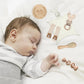 Une paisiblement endormie avec le Coffret Cadeau Naissance Bébé de BABY PREMA, entouré de peluches douces et d'accessoires bébé en bois.