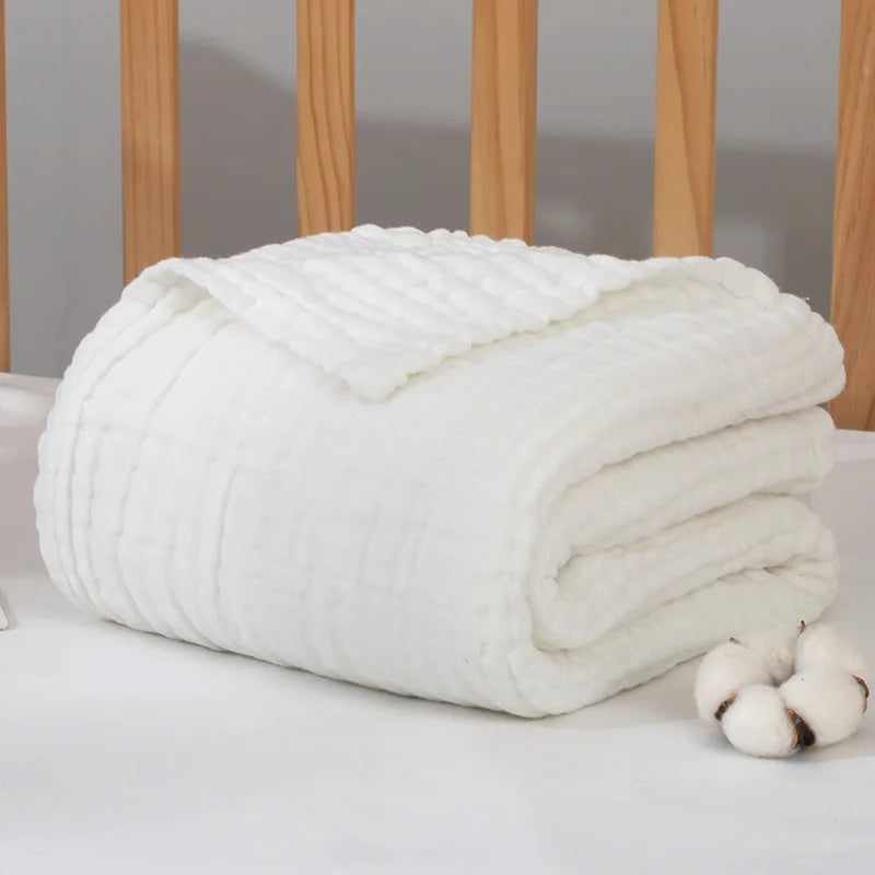 Une peluche blanche pliée Couvertures Mousseline | 6 Couches pour Nouveau-né sur un lit, conçues comme un accessoire bébé indispensable, à l'esthétique minimaliste et cosy par BABY PREMA.