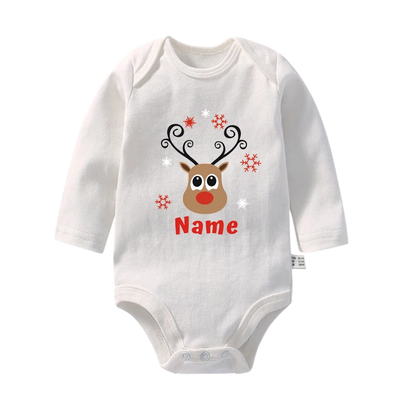 Une combinaison blanche pour bébé avec un joli visage de renne avec des bois, un nez rouge et de grands yeux. Cet adorable Body Noël Personnalisé pour Bébé de BABY-PREMA est décoré de flocons de neige rouges et blancs, et le mot « Nom » est imprimé sous le renne en lettres rouges, parfait pour les fêtes !