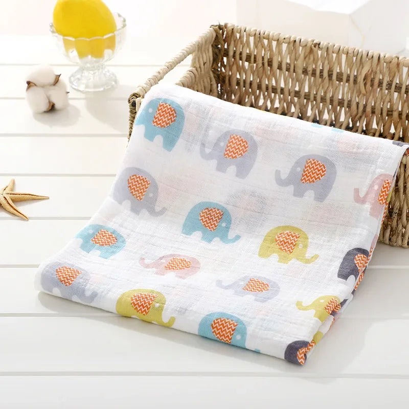 Une couverture pour bébé BABY PREMA en coton doux avec un motif d'éléphant coloré, drapée avec désinvolture sur le côté d'un panier tressé, dans un décor de chambre d'enfant lumineux et aéré pour un enfant.