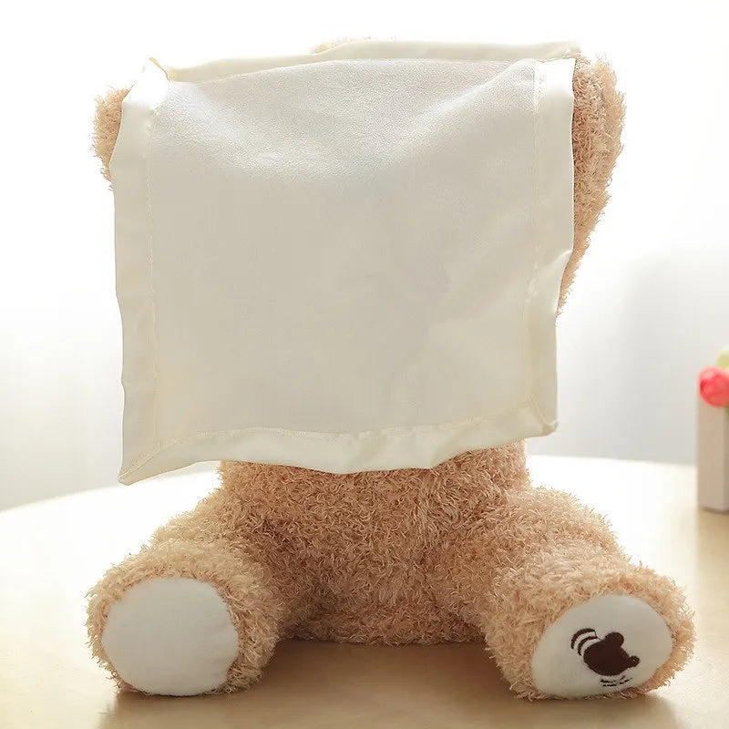 Un Doudou Ours Peluche Chantant Musical "Coucou" de BABY PREMA assis dos à la caméra, recouvert avec humour d'une couverture blanche drapée sur sa tête, créant une sensation ludique de cache-cache pour un enfant au dodo.