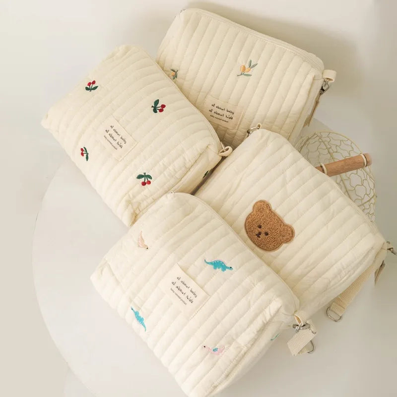 Quatre pochettes en tissu matelassé BABY PREMA avec de jolies broderies et étiquettes d'animaux, disposées élégamment sur une surface claire, parfaites pour les petits trésors de mon bébé.