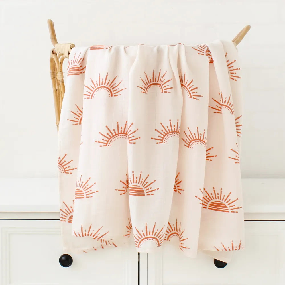 Une couverture rose BABY PREMA douillette avec un joyeux motif de soleil, parfaite pour bébé dodo, drapée sur une échelle en bois contre un mur blanc.