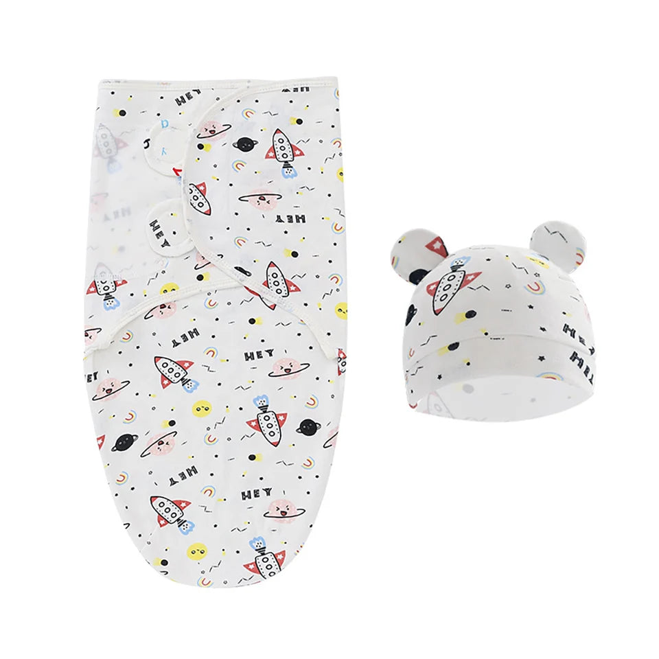 Un emmaillotage blanc pour bébé et un bonnet assorti avec un imprimé coloré sur le thème de l'espace, représentant des fusées, des planètes et des étoiles, avec de jolis détails d'oreilles sur le chapeau. Cette Couverture Bébé Emmaillotage | 0-6 Mois 2 Pièces de BABY PREMA est parfait pour