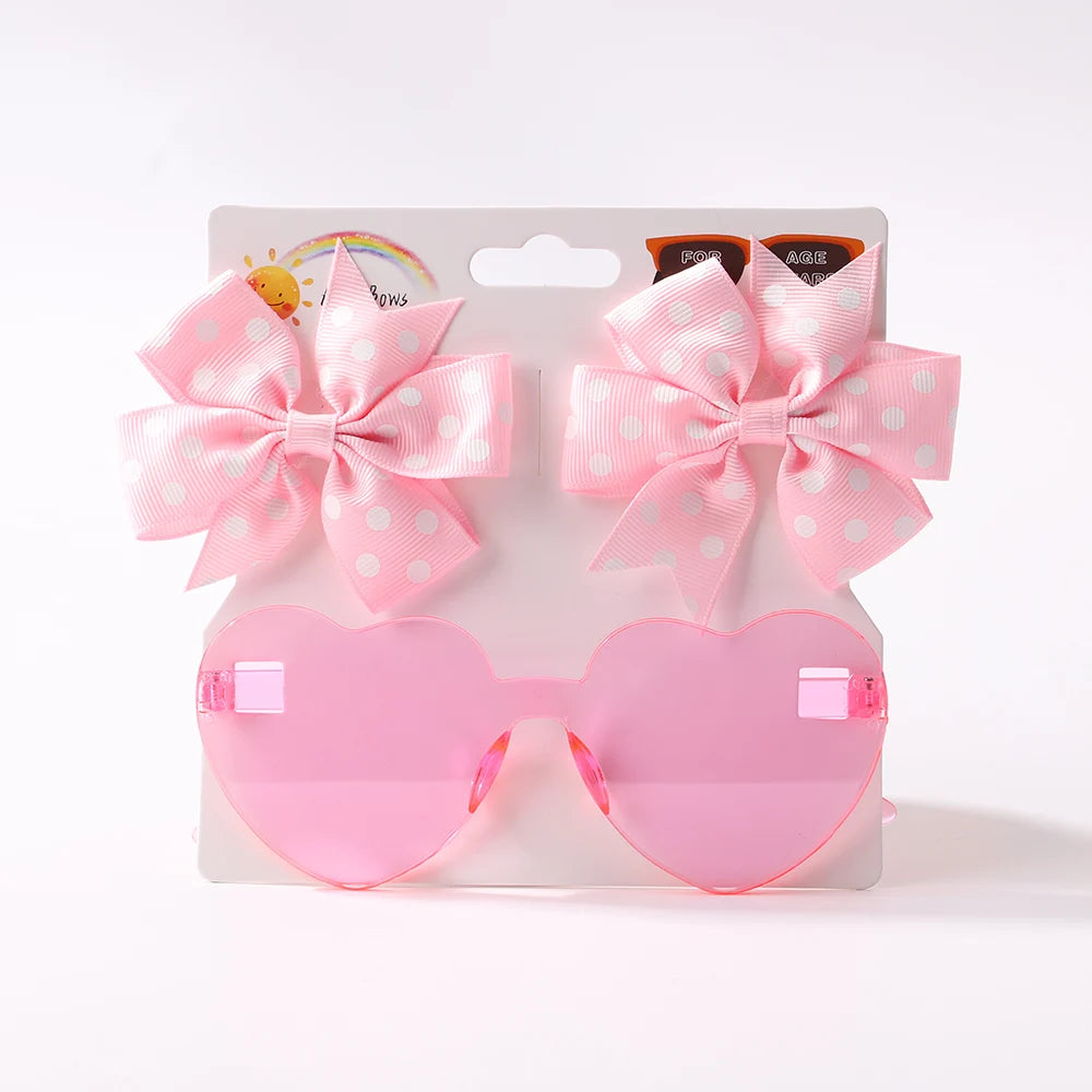 Ensemble d'Accessoires Bébé rose en forme de coeur | Les Lunettes de Cheveux pour Bébé de BABY PREMA sont associées à deux nœuds pour cheveux à pois roses, le tout affiché sur un fond blanc.