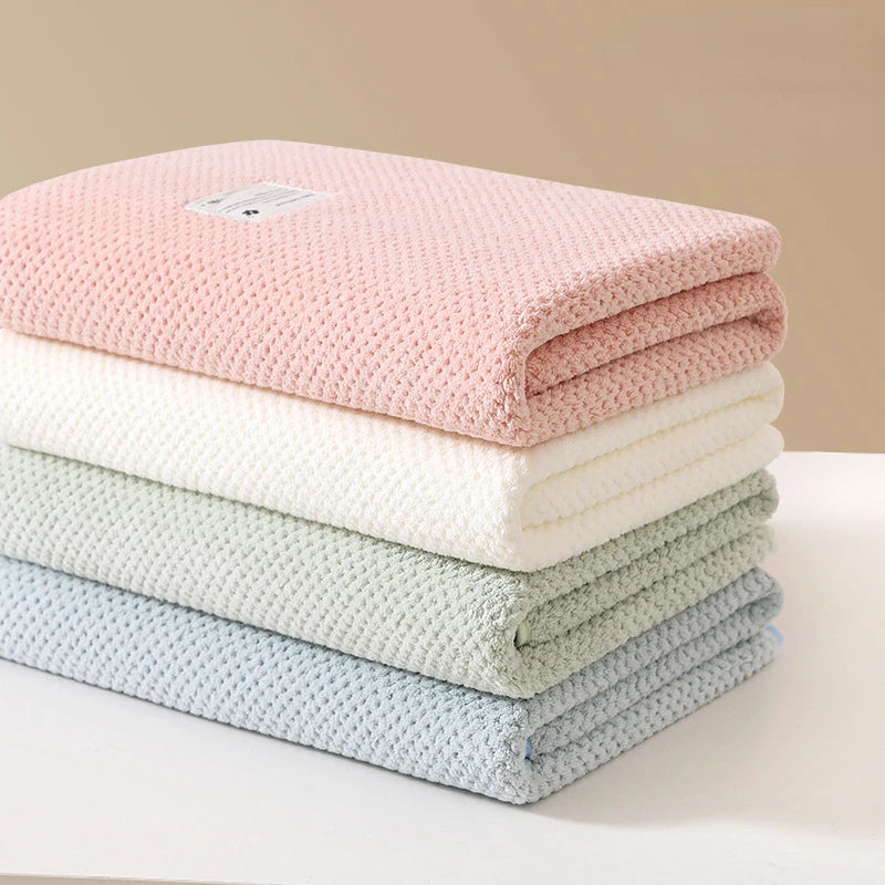 Une pile de serviettes BABY PREMA légères et soigneusement pliées dans des tons pastel de rose, blanc, vert et bleu sur une surface de couleur claire.