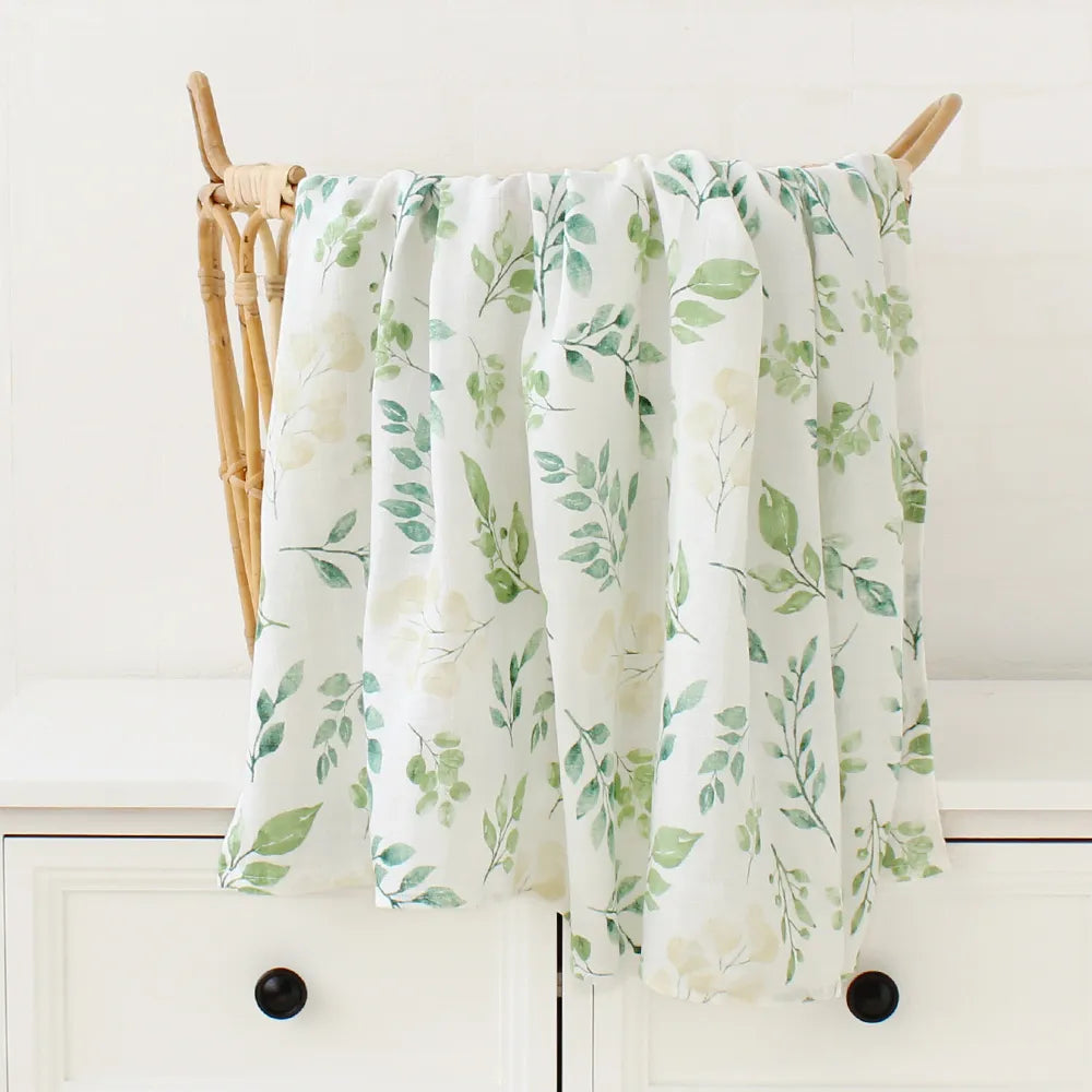 Un torchon floral aux motifs de feuilles vertes est drapé sur une cheville en bois, servant de Couverture Bébé en Coton et Bambou Bio de BABY PREMA, avec des armoires de cuisine de couleur claire en arrière-plan.