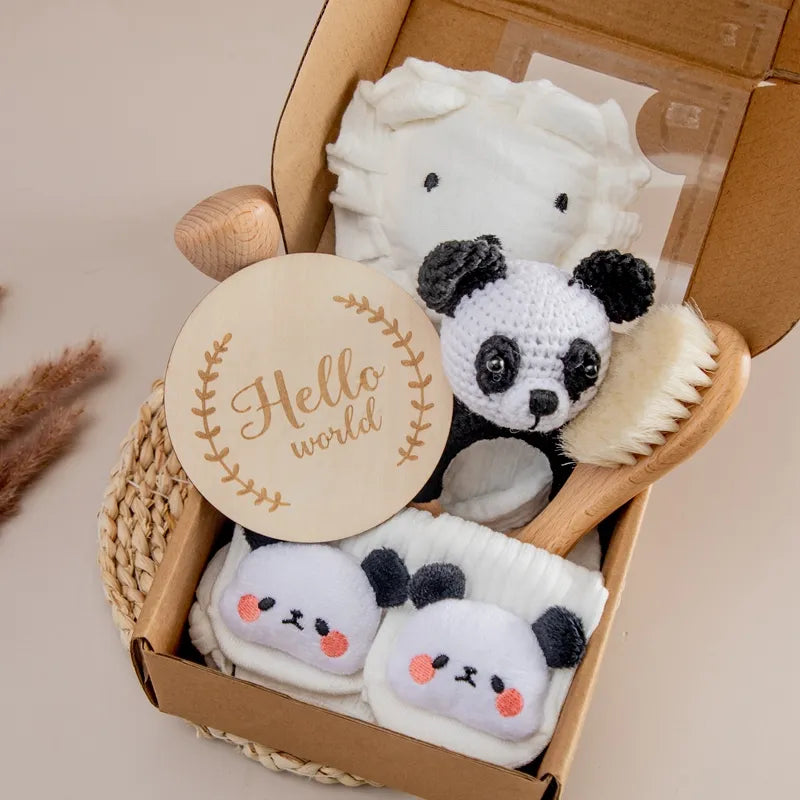 Un charmant coffret cadeau Coffret Cadeau Naissance Bébé de BABY PREMA comprenant des articles sur le thème du panda dans une boîte ouverte, comprenant un souvenir en bois « hello world », un jouet en peluche panda et de jolis chaussons à tête de panda.